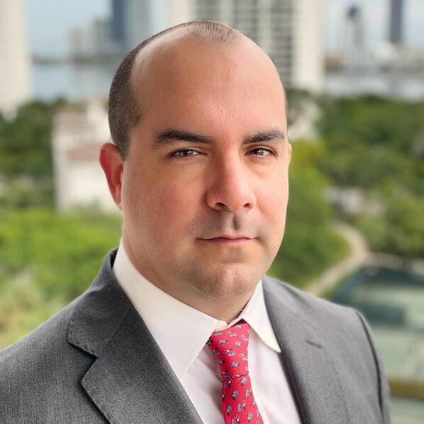 A man in a suit and tie standing next to trees.