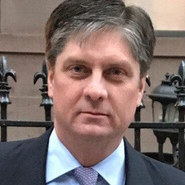 A man in suit and tie standing next to black fence.